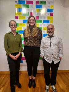 Two women and a man standing together for a photo in front of a wall.